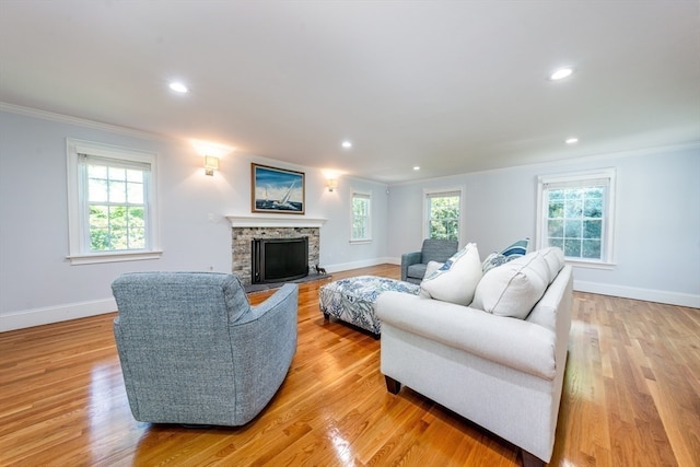 living room featuring a stone fireplace, light hardwood / wood-style flooring, and ornamental molding