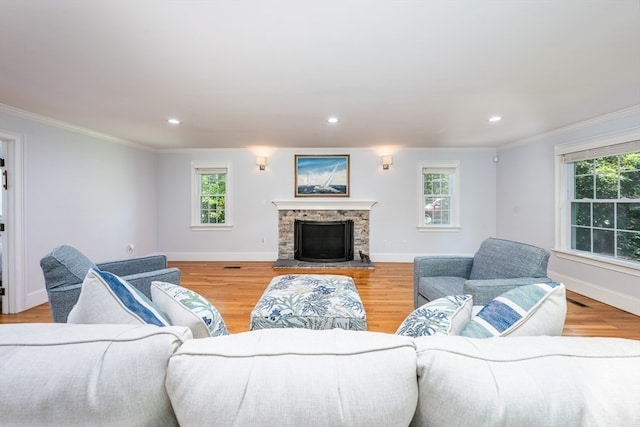 living room featuring a stone fireplace, crown molding, hardwood / wood-style floors, and plenty of natural light