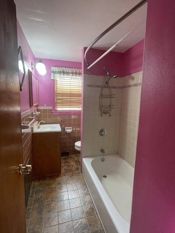 full bathroom with tiled shower / bath, vanity, toilet, and tile walls