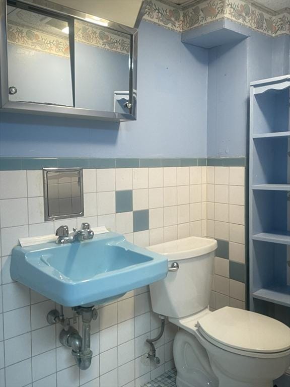 bathroom with toilet, sink, and tile walls