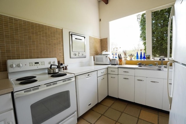 kitchen featuring white appliances, white cabinetry, a wealth of natural light, and light countertops