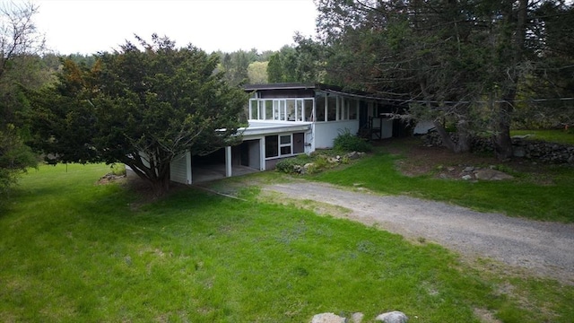back of property featuring a sunroom, a yard, driveway, and a carport