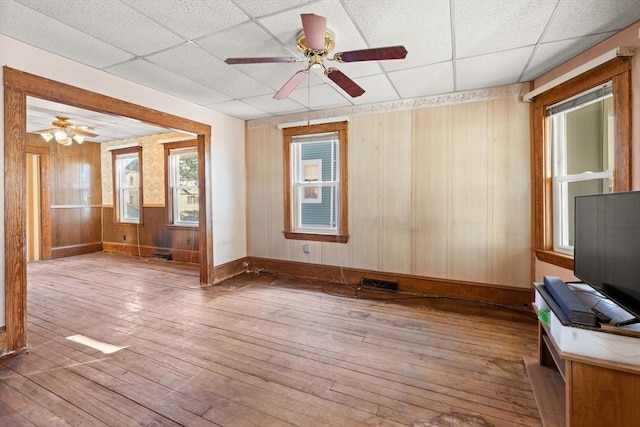 unfurnished room featuring wooden walls, wood-type flooring, a drop ceiling, and visible vents