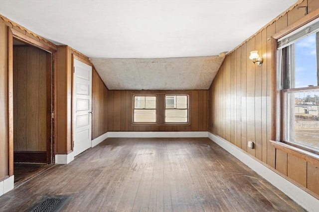 additional living space featuring lofted ceiling, visible vents, hardwood / wood-style floors, wood walls, and baseboards