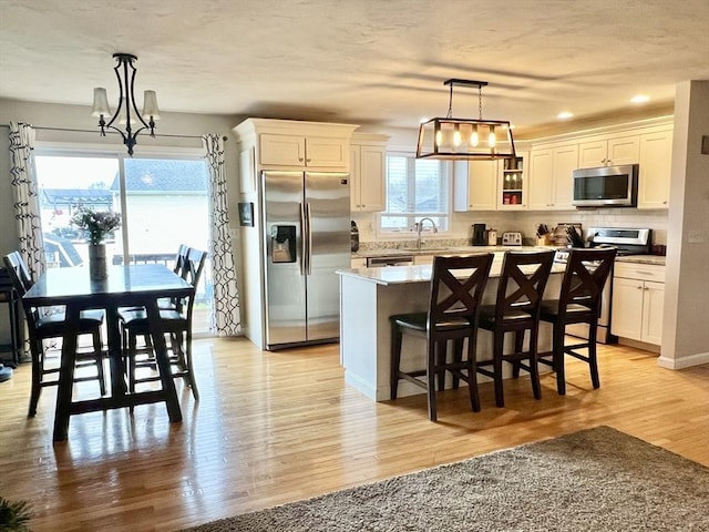 kitchen with plenty of natural light, light hardwood / wood-style floors, stainless steel appliances, and decorative light fixtures