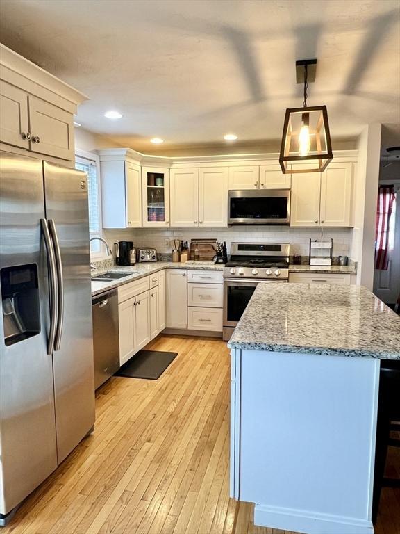 kitchen with sink, light stone counters, pendant lighting, appliances with stainless steel finishes, and light wood-type flooring