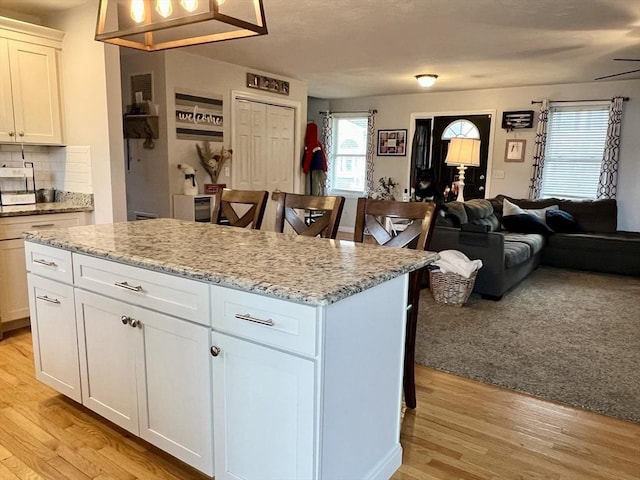 kitchen with tasteful backsplash, white cabinetry, a kitchen island, and light wood-type flooring