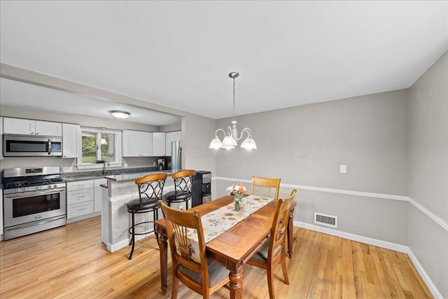 dining space with a chandelier, light wood finished floors, baseboards, and visible vents