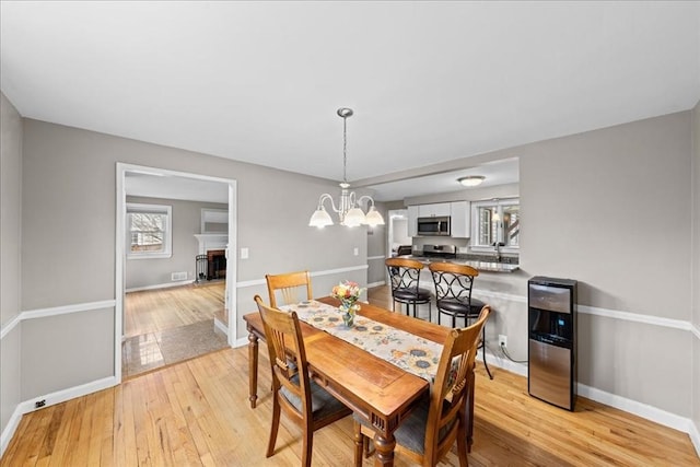 dining space featuring an inviting chandelier, a fireplace, light wood-type flooring, and baseboards