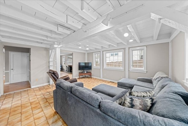 living area with track lighting, beamed ceiling, baseboards, and light tile patterned floors