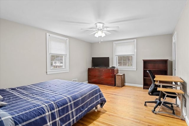 bedroom with a ceiling fan, wood finished floors, baseboards, and multiple windows