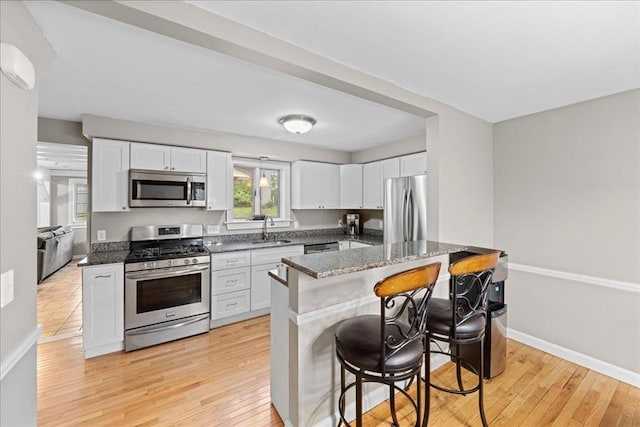 kitchen featuring light wood-style floors, a kitchen bar, a wall unit AC, stainless steel appliances, and a sink