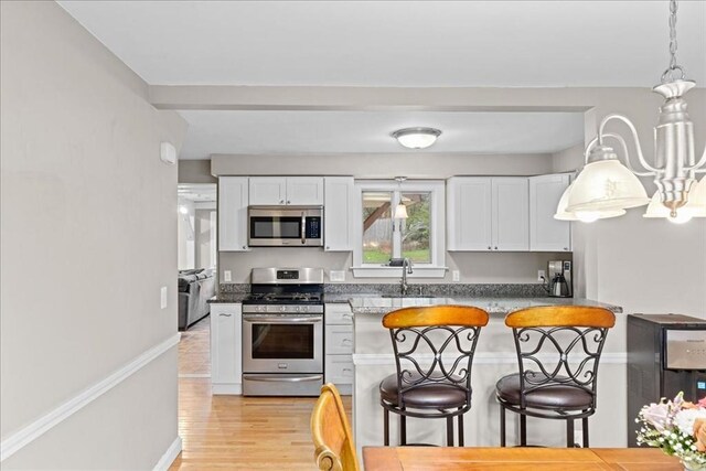 kitchen with light wood finished floors, white cabinetry, a kitchen breakfast bar, and stainless steel appliances