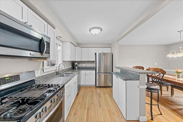 kitchen featuring white cabinets, a sink, appliances with stainless steel finishes, light wood finished floors, and a breakfast bar area