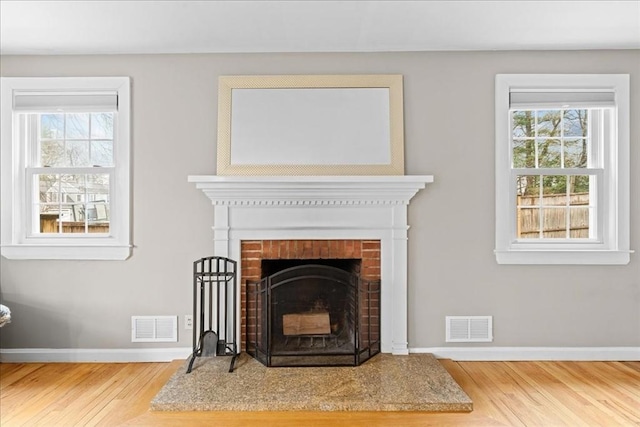 room details with a brick fireplace, visible vents, baseboards, and wood finished floors