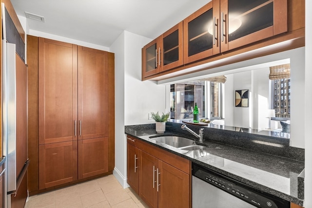 kitchen with dark stone countertops, sink, light tile patterned floors, and stainless steel dishwasher