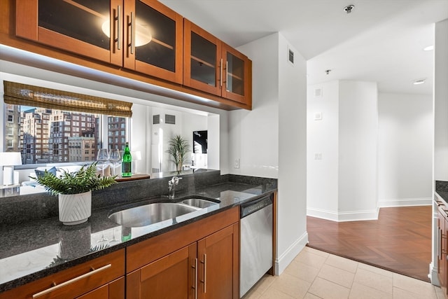 kitchen with stainless steel dishwasher, sink, dark stone counters, and light parquet floors