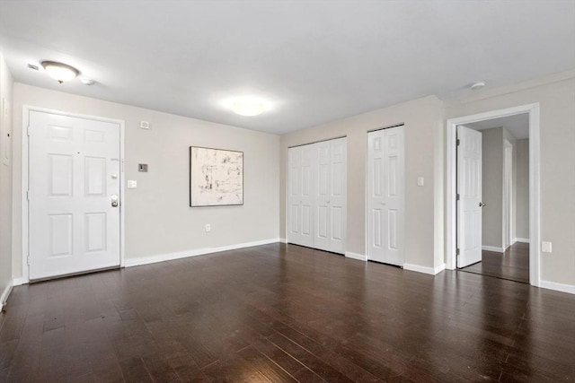 unfurnished living room featuring dark wood-type flooring and baseboards