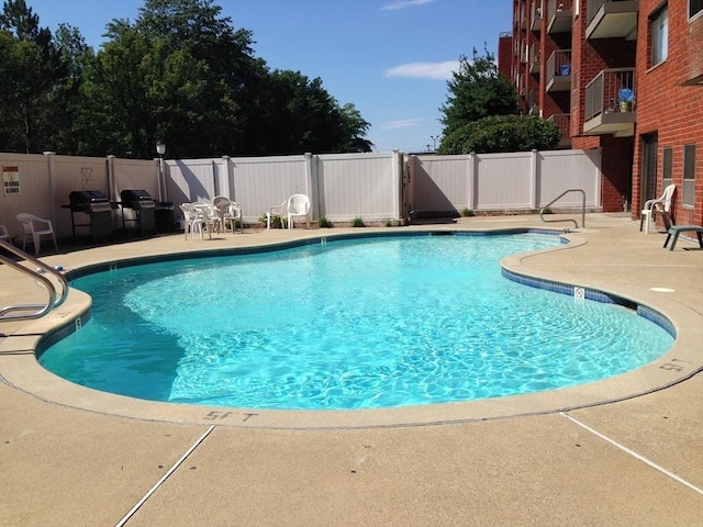 community pool with a patio, fence, and area for grilling