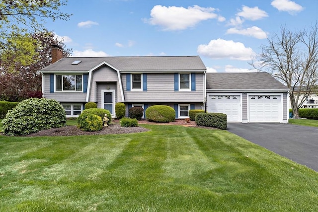raised ranch featuring a chimney, asphalt driveway, a garage, and a front yard
