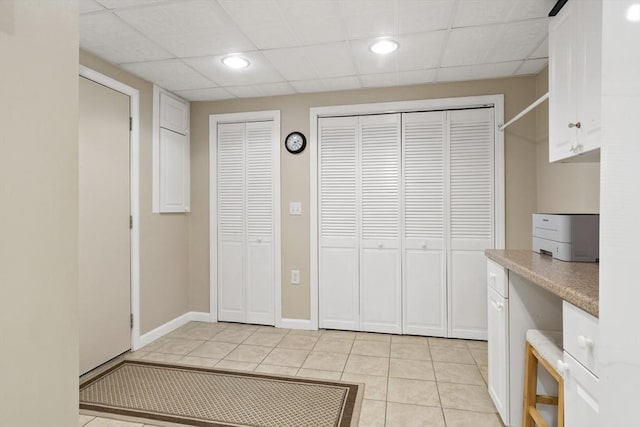 interior space featuring light tile patterned flooring, a paneled ceiling, and baseboards