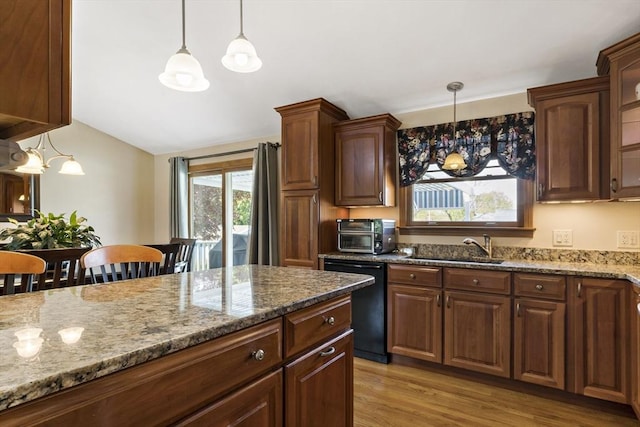 kitchen featuring black dishwasher, a sink, light stone countertops, vaulted ceiling, and decorative light fixtures