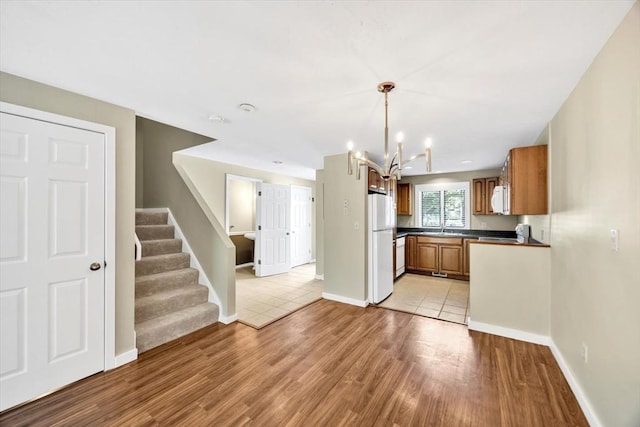 kitchen with white appliances, brown cabinets, light wood finished floors, dark countertops, and decorative light fixtures