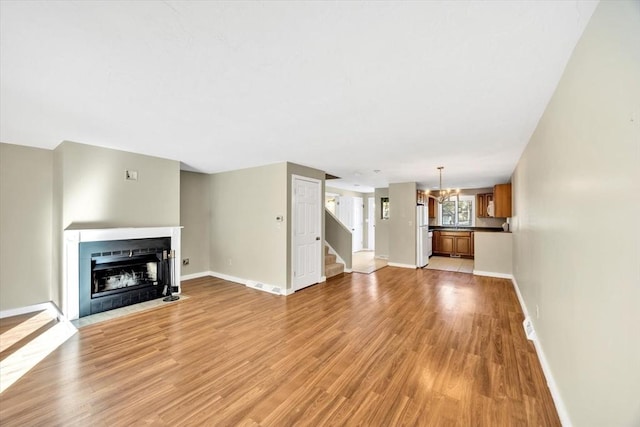 unfurnished living room featuring light wood-style floors, a fireplace with flush hearth, stairway, and baseboards