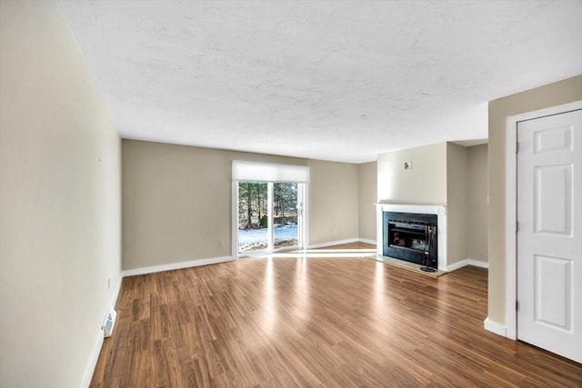 unfurnished living room with a fireplace with flush hearth, visible vents, baseboards, and wood finished floors