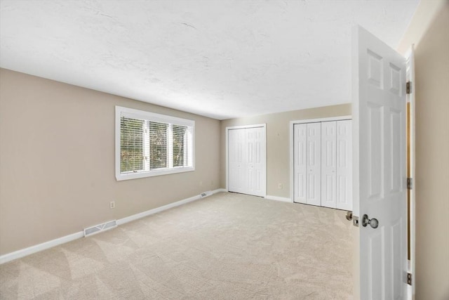 unfurnished bedroom with multiple closets, visible vents, light carpet, a textured ceiling, and baseboards