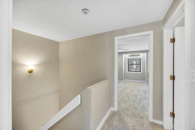 corridor with light carpet, baseboards, and an upstairs landing