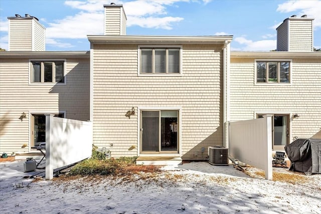 snow covered property featuring entry steps, fence, a chimney, and central air condition unit