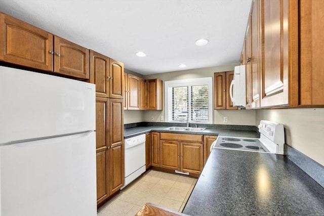 kitchen with white appliances, light tile patterned floors, dark countertops, brown cabinets, and a sink