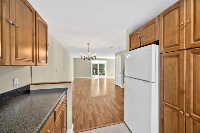 kitchen featuring light wood finished floors, brown cabinets, freestanding refrigerator, a chandelier, and pendant lighting