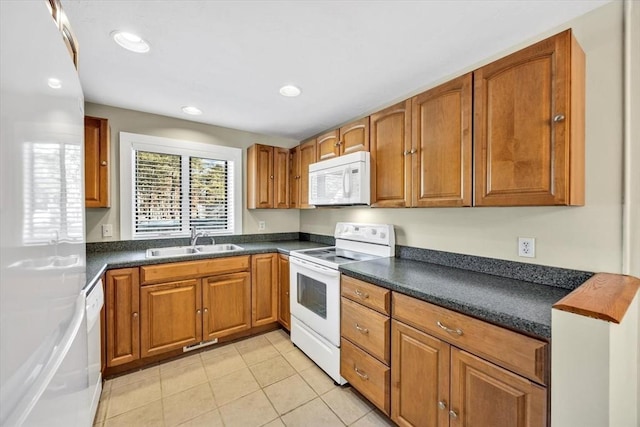 kitchen featuring light tile patterned flooring, white appliances, a sink, brown cabinetry, and dark countertops