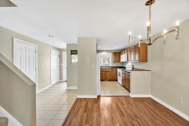 kitchen with white appliances, light tile patterned floors, baseboards, brown cabinetry, and dark countertops