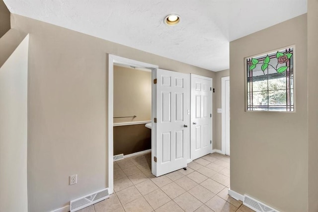 corridor featuring light tile patterned floors, baseboards, and visible vents