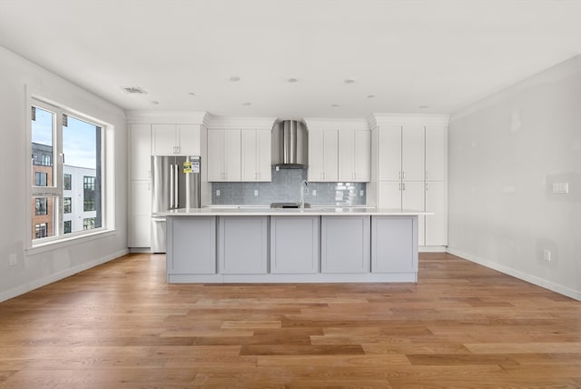 kitchen featuring light hardwood / wood-style floors, wall chimney range hood, decorative backsplash, and a center island with sink