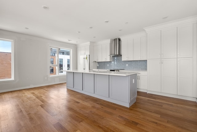 kitchen with light hardwood / wood-style flooring, a healthy amount of sunlight, a center island with sink, and wall chimney range hood