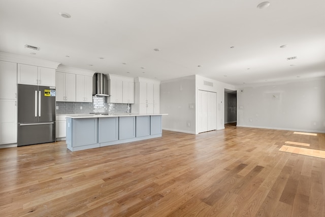 kitchen with white cabinetry, light wood-type flooring, wall chimney exhaust hood, a center island, and stainless steel refrigerator