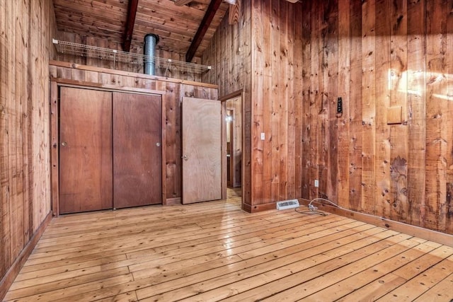 spare room featuring beamed ceiling, light wood-style flooring, and wooden walls