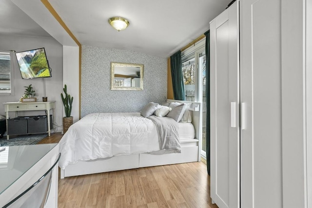 bedroom with light wood-style floors, an accent wall, and wallpapered walls