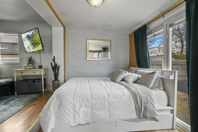 bedroom with wallpapered walls, an accent wall, and wood finished floors