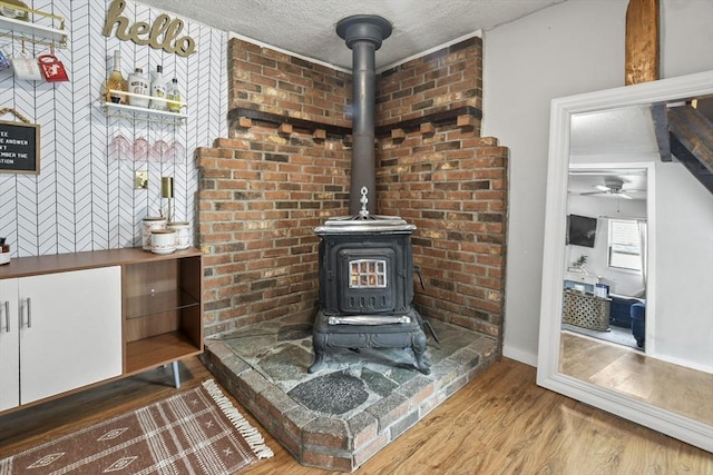 interior details featuring a ceiling fan, a wood stove, wood finished floors, and a textured ceiling