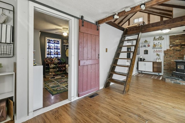 interior space with visible vents, a textured ceiling, wood finished floors, a barn door, and a wood stove