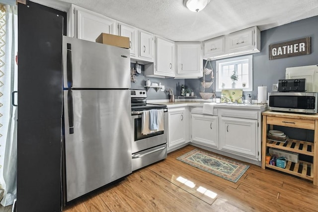 kitchen featuring light wood-type flooring, light countertops, appliances with stainless steel finishes, a textured ceiling, and white cabinetry