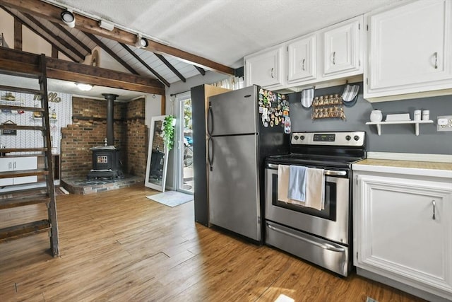 kitchen featuring hardwood / wood-style floors, a wood stove, vaulted ceiling with beams, stainless steel appliances, and white cabinets