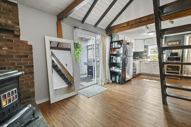 kitchen with light wood finished floors, a wood stove, vaulted ceiling with beams, appliances with stainless steel finishes, and white cabinetry