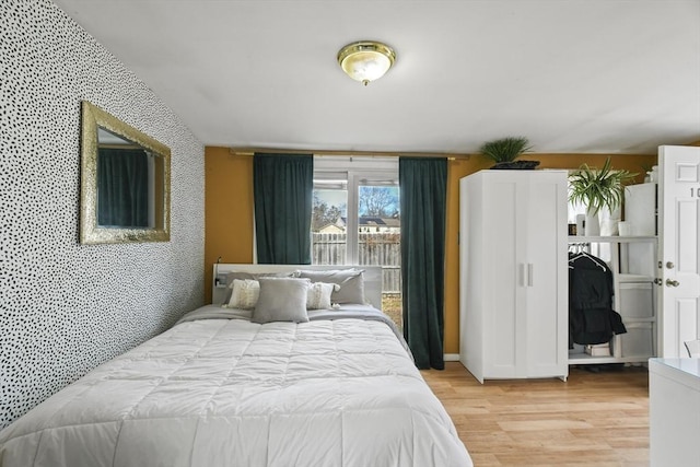 bedroom featuring light wood-style flooring, wallpapered walls, an accent wall, and baseboards