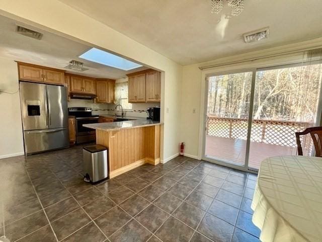 kitchen with sink, a skylight, kitchen peninsula, dark tile patterned flooring, and stainless steel appliances